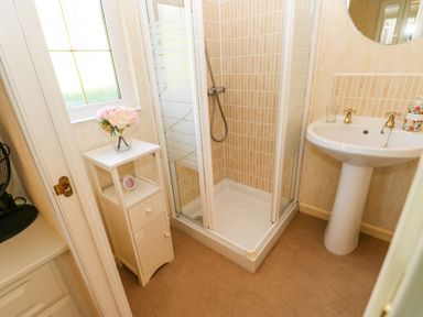 A bathroom with a shower, pedestal sink, small cabinet with flowers and window at The Fairhaven in Tunstall near Catterick North Yorkshire
