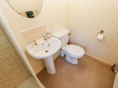 A bathroom with a pedestal sink, toilet, round mirror, and a shower at The Fairhaven in Tunstall near Catterick North Yorkshire