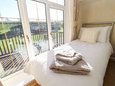 A bedroom with a single bed towels on the bed and glass doors opening to a balcony at The Fairhaven in Tunstall near Catterick North Yorkshire
