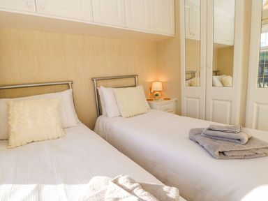A bedroom with two single beds white bedding bedside table and mirrored wardrobe at The Fairhaven in Tunstall near Catterick North Yorkshire