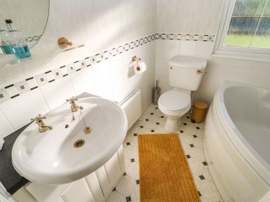 A bathroom with a toilet sink bathtub orange rug and window at The Fairhaven in Tunstall near Catterick North Yorkshire