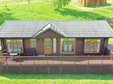 A wooden cabin with a porch and outdoor furniture surrounded by grass at The Fairhaven in Tunstall near Catterick North Yorkshire
