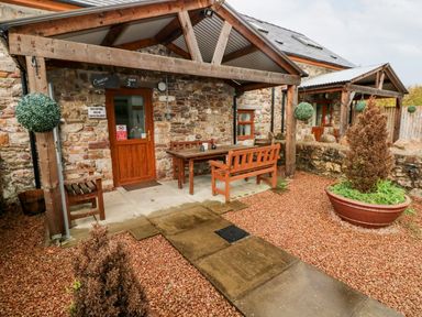 An outdoor seating area with wooden benches and a table under a wooden roof at Barn 2 in Ystradgynlais