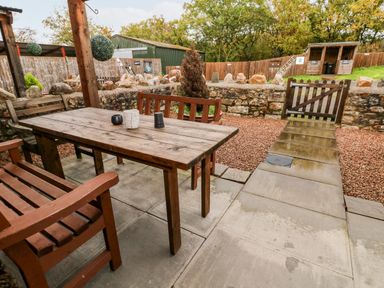 An outdoor patio area with a wooden table and benches surrounded by stone walls and a wooden gate at Barn 2 in Ystradgynlais