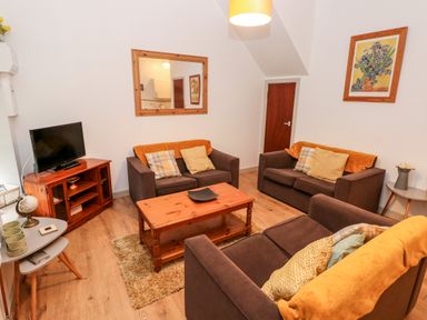 A living room with brown sofas, a wooden coffee table, a television on a wooden stand, and wall art at Barn 2 in Ystradgynlais