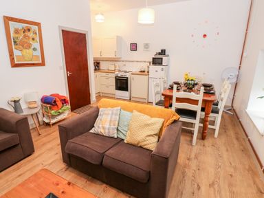 An open plan living room and kitchen with brown sofas and a dining table with chairs at Barn 2 in Ystradgynlais