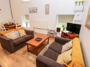 A living room with two brown sofas a wooden coffee table a television on a wooden stand and a dining table with chairs at Barn 2 in Ystradgynlais