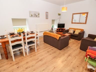 A living room with brown sofas a wooden dining table with chairs and a television at Barn 2 in Ystradgynlais