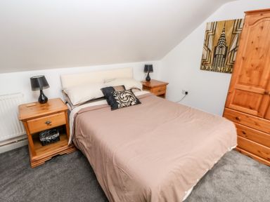 A bedroom with a bed between two wooden nightstands with lamps and a wooden wardrobe at Barn 2 Ystradgynlais