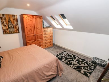 A bedroom with a bed wardrobe chest of drawers skylight windows and a rug at Barn 2 Ystradgynlais