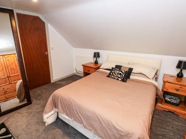 A bedroom with a bed between two wooden nightstands each with a lamp and a large mirror reflecting a wooden wardrobe at Barn 2 in Ystradgynlais