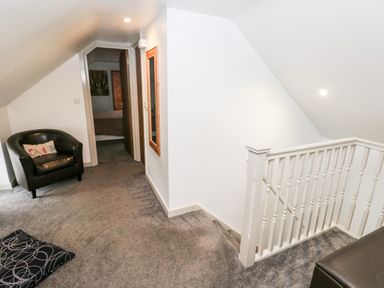 A carpeted upstairs landing with a black armchair and stairs with white railing at Barn 2 Ystradgynlais