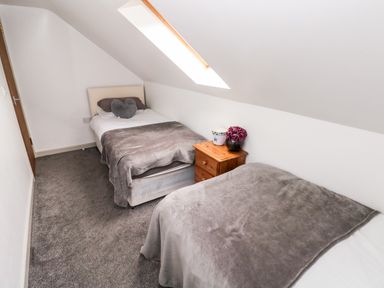 A bedroom with two single beds a wooden nightstand with flowers and a skylight window at Barn 2 Ystradgynlais