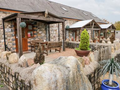 Exterior of stone cottages with wooden porches and outdoor seating areas at Barn 2 in Ystradgynlais