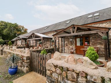 The exterior of stone cottages with wooden gates and small patios at Barn 2 in Ystradgynlais