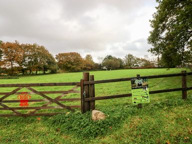 A wooden fence with a gate and a sign next to a green field with trees in the background at Barn 2 in Ystradgynlais