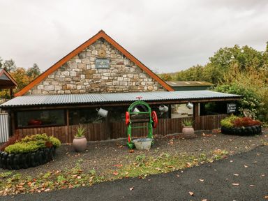 The exterior of a stone long house with a corrugated metal roof and garden beds made from tires at Barn 2 in Ystradgynlais