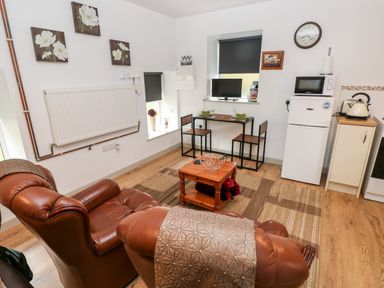 A living area with two leather chairs a wooden table with two chairs a small fridge and microwave at Barn 3 Cwm-twrch Isaf near Ystradgynlais