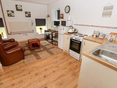 A kitchen and living area with leather armchairs a dining table small refrigerator and stove at Barn 3 Cwm-twrch Isaf near Ystradgynlais