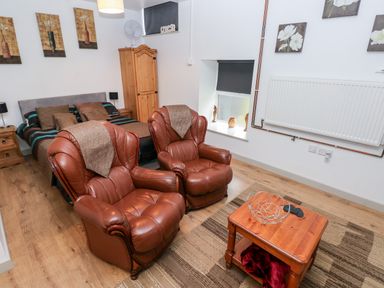 A bedroom with two brown leather armchairs next to a wooden coffee table and a double bed at Barn 3 in Cwm-twrch Isaf near Ystradgynlais