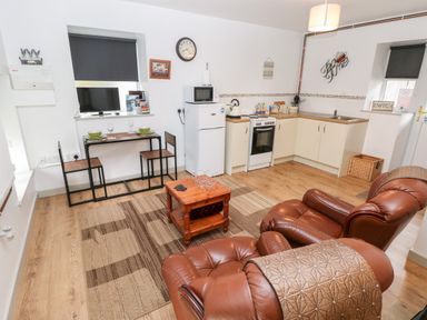 A kitchen and living area with brown leather chairs a small wooden table a dining table with chairs and kitchen appliances at Barn 3 in Cwm-twrch Isaf near Ystradgynlais