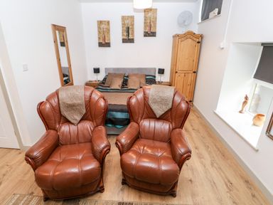 A bedroom with two brown leather armchairs a bed with pillows and artwork above at Barn 3 in Cwm-twrch Isaf near Ystradgynlais