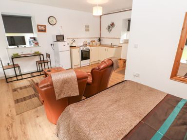 A small kitchen and living area with two brown chairs a table a bed and a dining table at Barn 3 in Cwm-twrch Isaf near Ystradgynlais