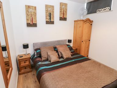 A bedroom with a double bed cushions bedside tables lamps a wooden wardrobe a mirror and wall art at Barn 3 Cwm-twrch Isaf near Ystradgynlais