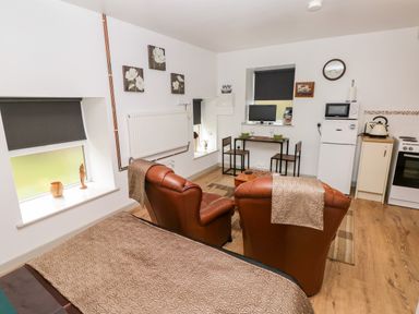 A small living area with two brown leather chairs a bed a dining table with two chairs a refrigerator a microwave and an oven at Barn 3 Cwm-twrch Isaf near Ystradgynlais