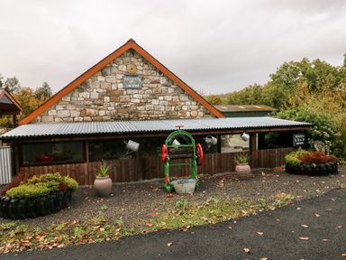 An exterior view of a stone building with a corrugated metal roof and wooden fence with planters and a green and red metal machine outside at Barn 3 in Cwm-twrch Isaf near Ystradgynlais