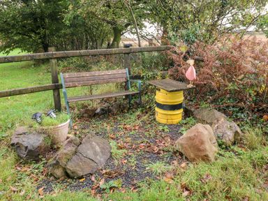 An outdoor seating area with a wooden bench yellow barrel table and rocks at Barn 3 Cwm-twrch Isaf near Ystradgynlais
