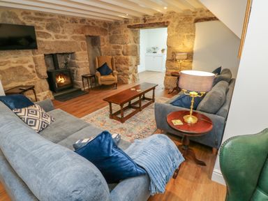 A living room with stone walls a wood burning stove sofas a wooden coffee table and table lamps at The Old Post Office in Praze-An-Beeble