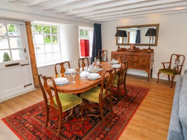 A dining room with a wooden table set with plates and glasses on a red patterned rug at The Old Post Office in Praze-An-Beeble