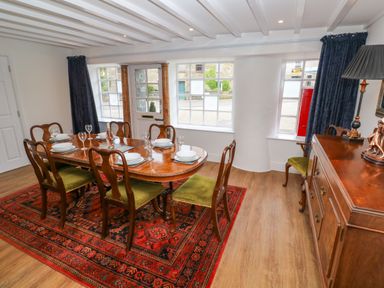 A dining room with a wooden table set with dishes and glasses surrounded by chairs on a patterned rug at The Old Post Office in Praze-An-Beeble