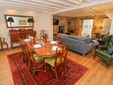 A dining room and living area with a wooden table and chairs a red patterned rug a gray sofa and a green armchair at The Old Post Office in Praze-An-Beeble