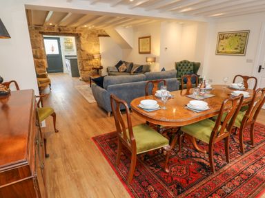 A dining area with wooden table and green chairs and a living area with blue sofas in a room with wooden floor at The Old Post Office in Praze-An-Beeble