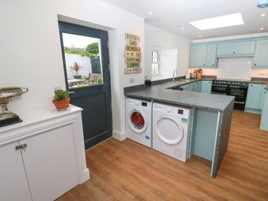 A kitchen with teal cabinets white appliances and a black door leading outside at The Old Post Office in Praze-An-Beeble