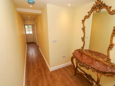 A narrow hallway with wooden floor and pale yellow walls with a decorative console table and mirror at The Old Post Office in Praze-An-Beeble