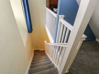 A carpeted staircase with white railings and a blue curtain at The Old Post Office in Praze-An-Beeble