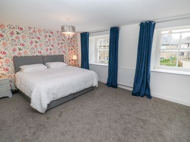 A bedroom with a double bed and floral wallpaper on one wall and blue curtains at The Old Post Office in Praze-An-Beeble