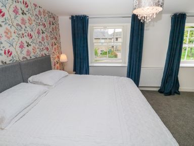 A bedroom with a bed white bedding floral wallpaper bedside lamp and blue curtains at The Old Post Office in Praze-An-Beeble