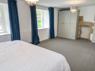 A bedroom with a white bedspread blue curtains a grey wardrobe and a stone fireplace at The Old Post Office in Praze-An-Beeble