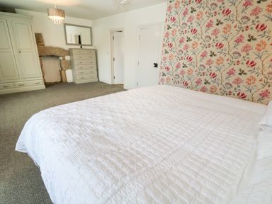 A bedroom with a bed covered in white bedding floral wallpaper wardrobe and dresser at The Old Post Office in Praze-An-Beeble