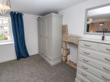 A bedroom with a gray wardrobe, gray chest of drawers, stone fireplace, blue curtains, and a window at The Old Post Office in Praze-An-Beeble