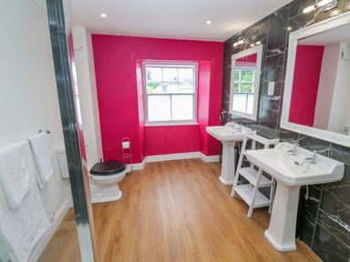 A bathroom with two pedestal sinks and mirrors a toilet with a black seat and a window with pink walls at The Old Post Office in Praze-An-Beeble