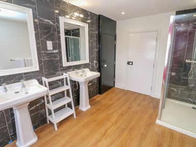 A bathroom with two pedestal sinks white framed mirrors a small white shelf unit a glass shower enclosure and wooden flooring at The Old Post Office in Praze-An-Beeble