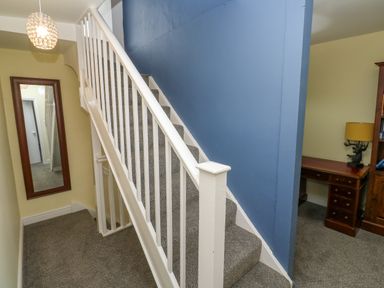 A carpeted staircase with white railing and blue wall beside a hallway with a mirror and a wooden desk with a lamp at The Old Post Office in Praze An Beeble
