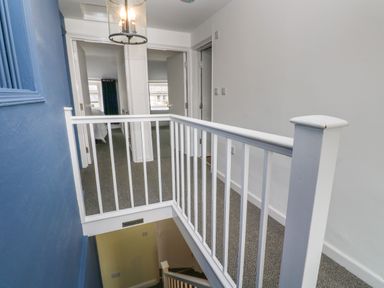 A hallway with white railing and carpet leading to rooms with open doors at The Old Post Office in Praze-An-Beeble