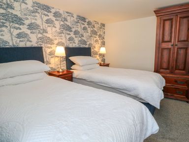 A bedroom with two beds bedside tables with lamps and a wooden wardrobe at The Old Post Office in Praze-An-Beeble
