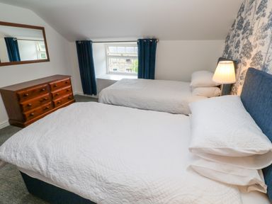A bedroom with two beds white bedding a wooden dresser a mirror and a window with blue curtains at The Old Post Office in Praze-An-Beeble